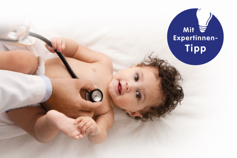 Alt-Tag: Ein Arzt untersucht ein lächelndes Baby mit einem Stethoskop auf einer Liege.