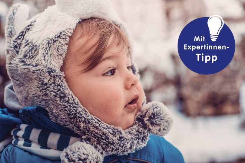 Kleines Kind mit einem kuscheligen, tierähnlichen Winterhut und blauer Jacke, im Freien in winterlicher Umgebung.
