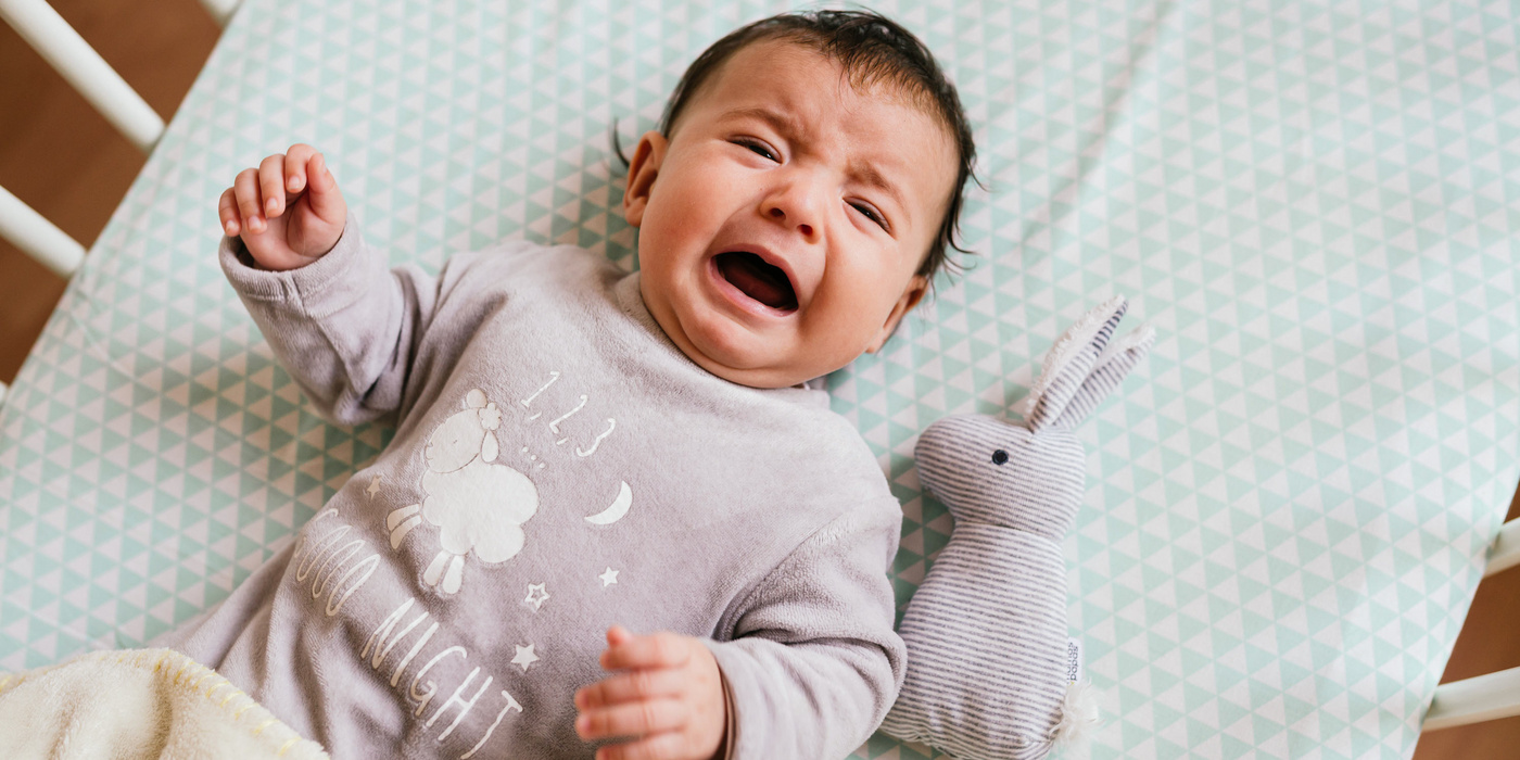 Humana Baby liegt im Bett und weint