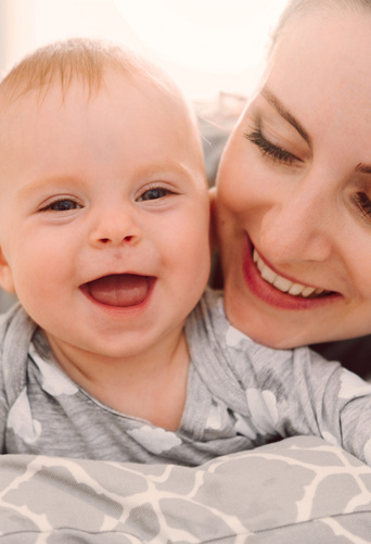 happy smiling mother and baby playing on bed at home