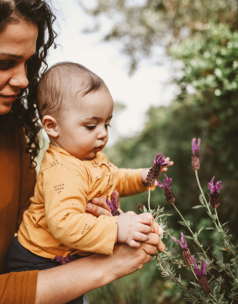 Humana Baby pflückt Blumen mit Mama