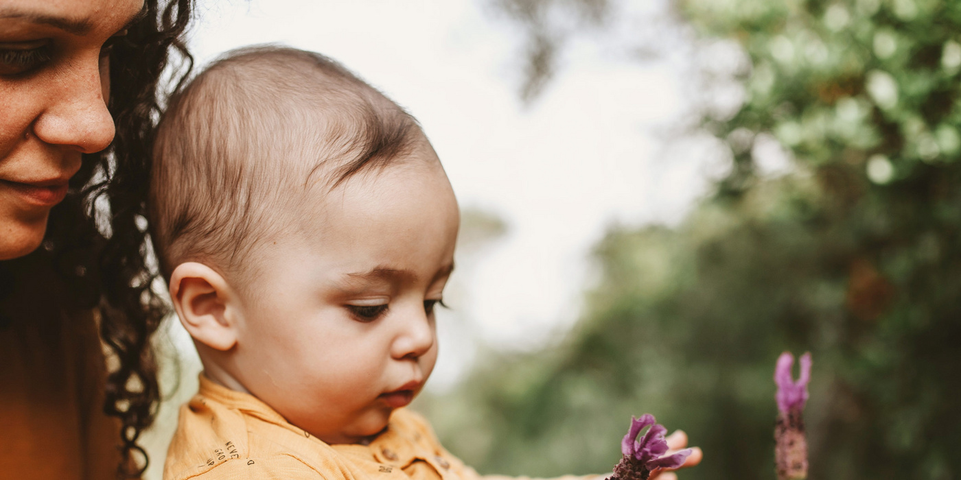 Humana Baby pflückt Blumen mit Mama