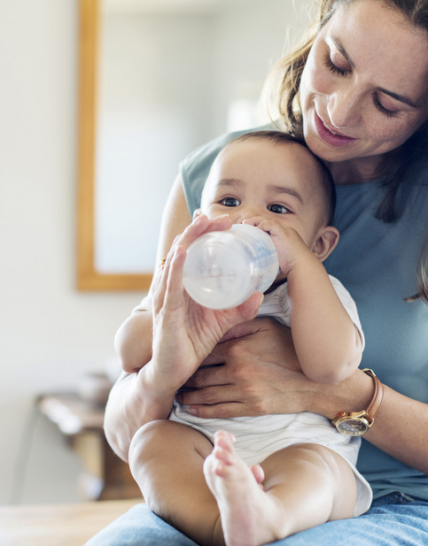 Humana Baby trinkt aus Flasche auf Mamas Schoß