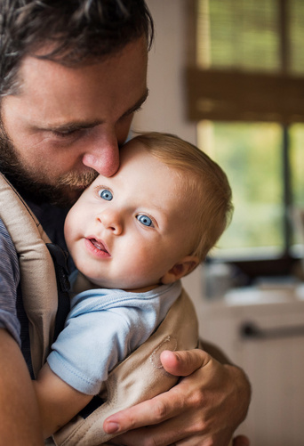 Humana Papa trägt Baby an seiner Brust