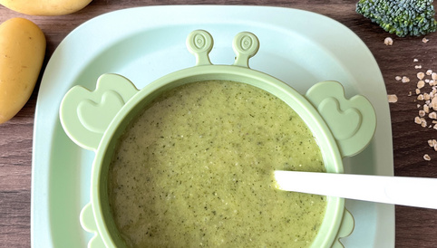 Grüner Broccoli-Kartoffelbrei in einer kindgerechten Schüssel auf einem Holztisch, umgeben von Kartoffeln, Brokkoli und Haferflocken.