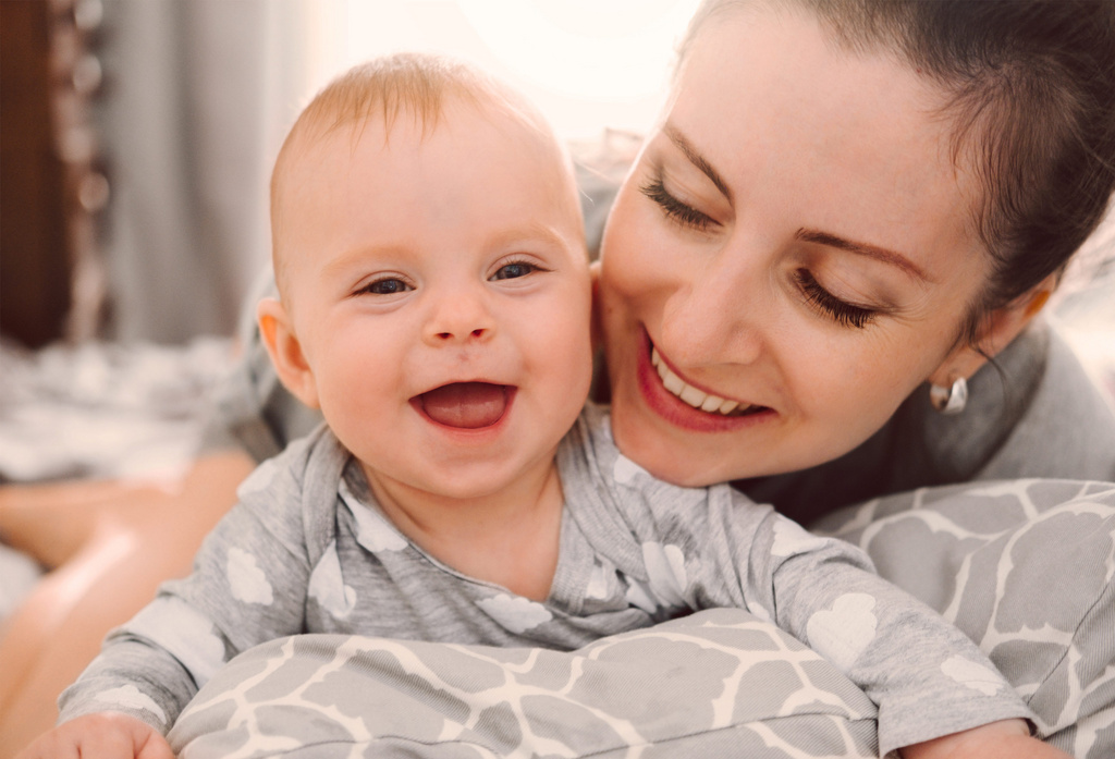 Humana glückliche Mutter und Baby spielen im Bett