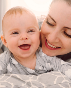 Humana glückliche Mutter und Baby spielen im Bett