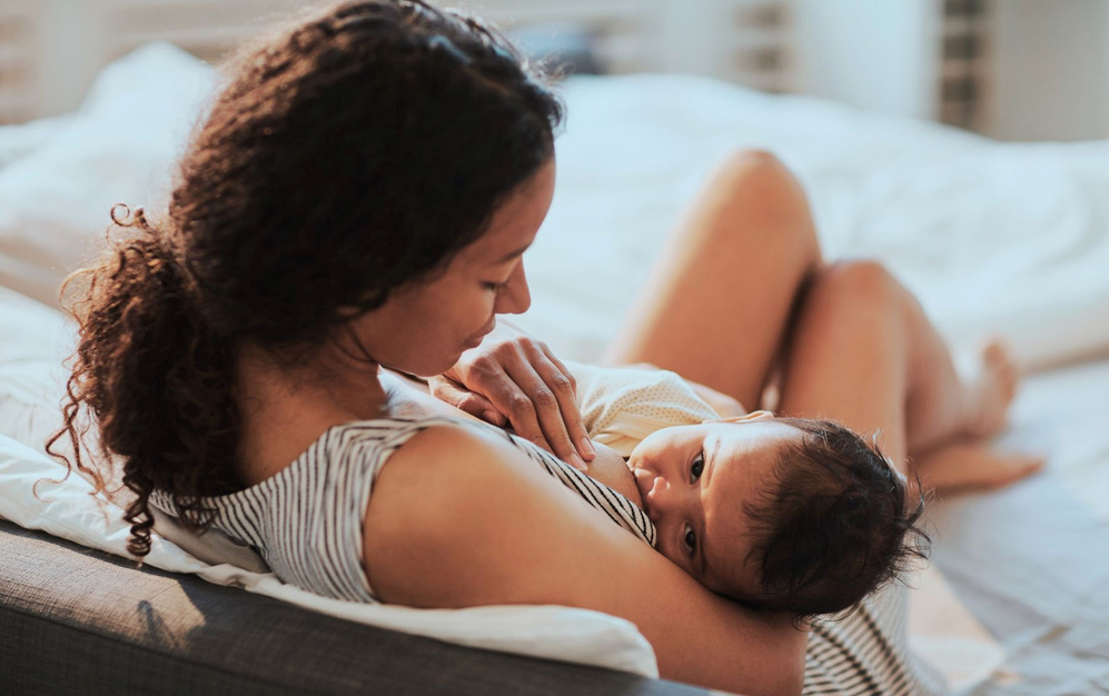 Mutter stillt ihr Baby auf dem Bett, beide wirken entspannt und zufrieden.