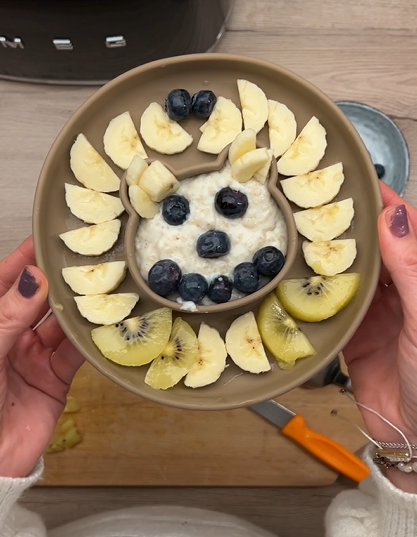 Bowl mit Haferbrei, dekoriert mit Bananen- und Kiwi-Scheiben, sowie Heidelbeeren, auf einem Holzuntergrund.