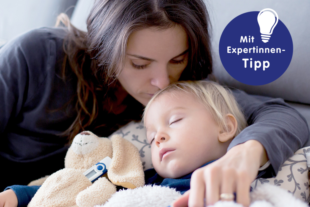 Mutter küsst schlafendes Kind, das einen kuscheligen Hund hält, mit einem Experten-Tipp zu Erkältung