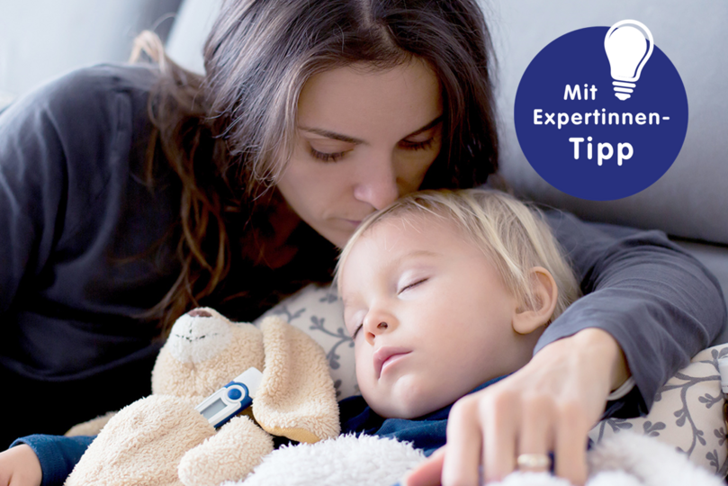 Mutter küsst schlafendes Kind, das einen kuscheligen Hund hält, mit einem Experten-Tipp zu Erkältung