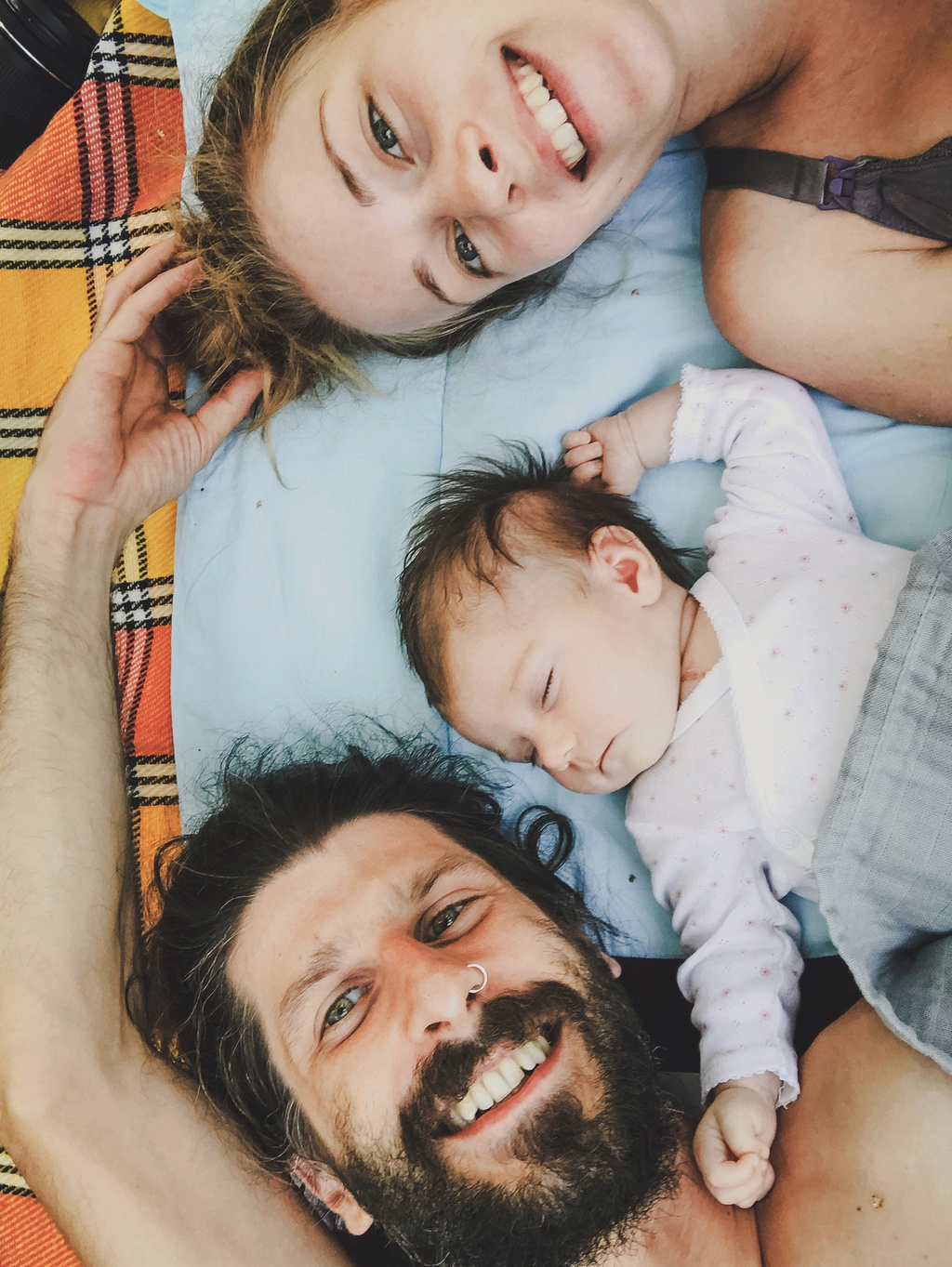 Paar liegt lachend auf einer Decke neben einem schlafenden Baby.